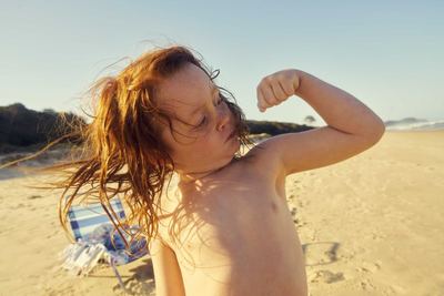 a shirtless young man flexing his muscles on the beach