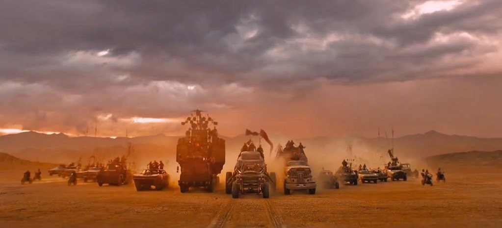 a group of vehicles driving through a desert under a cloudy sky