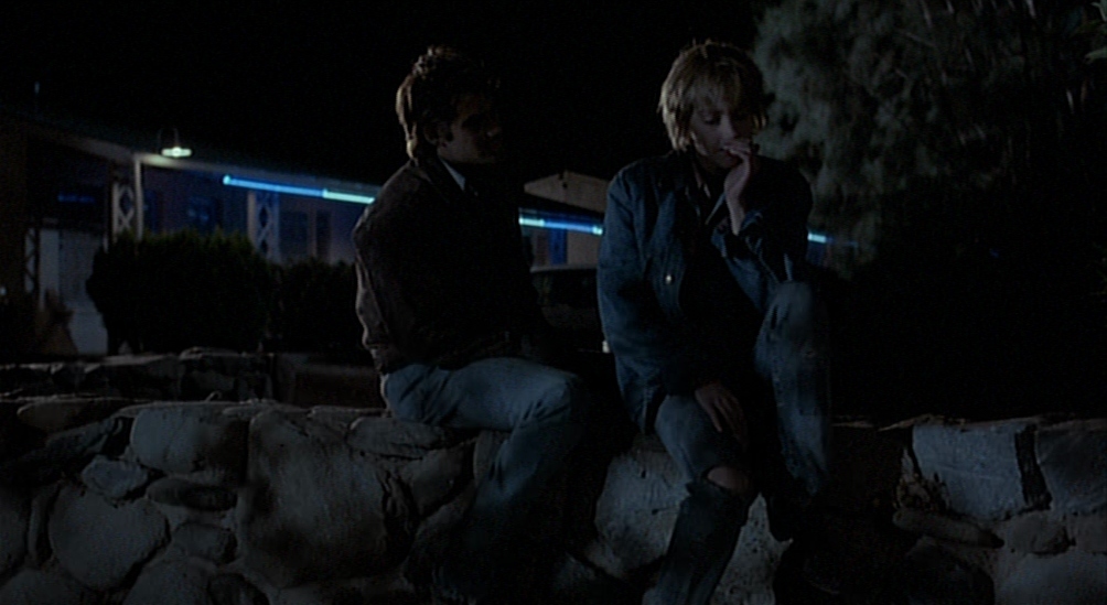 two people sitting on a rock wall at night