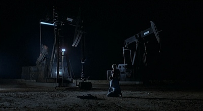 a person walking in the dark near some oil pumps