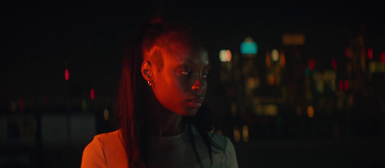 a woman standing in the dark with a city in the background