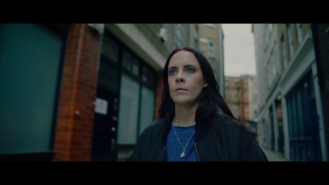 a woman in a blue shirt and black jacket standing in front of a building