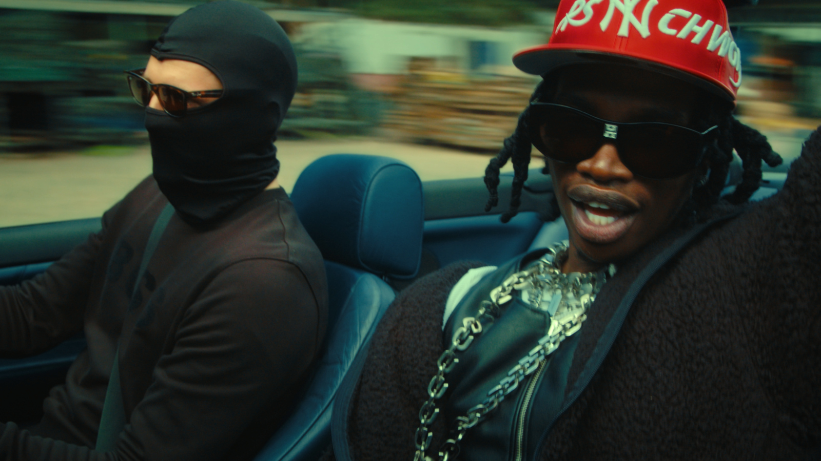 a man wearing a red hat and a bandana driving a car