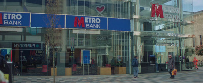 a man walking down a street past a metro bank