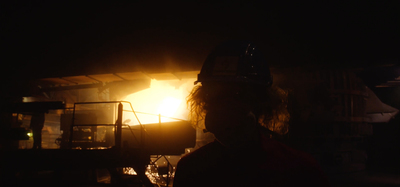 a man in a hard hat standing in front of a fire