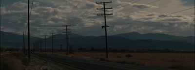 an empty road with power lines and mountains in the background