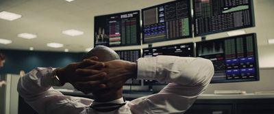 a man in a white shirt and tie sitting in front of a wall of stock