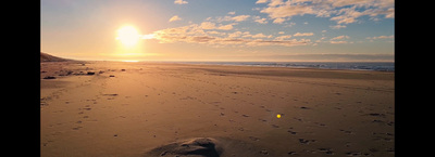 the sun is setting on the beach with footprints in the sand