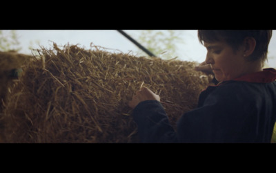 a young boy standing next to a pile of hay