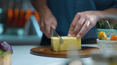 a person cutting a block of cheese with a knife