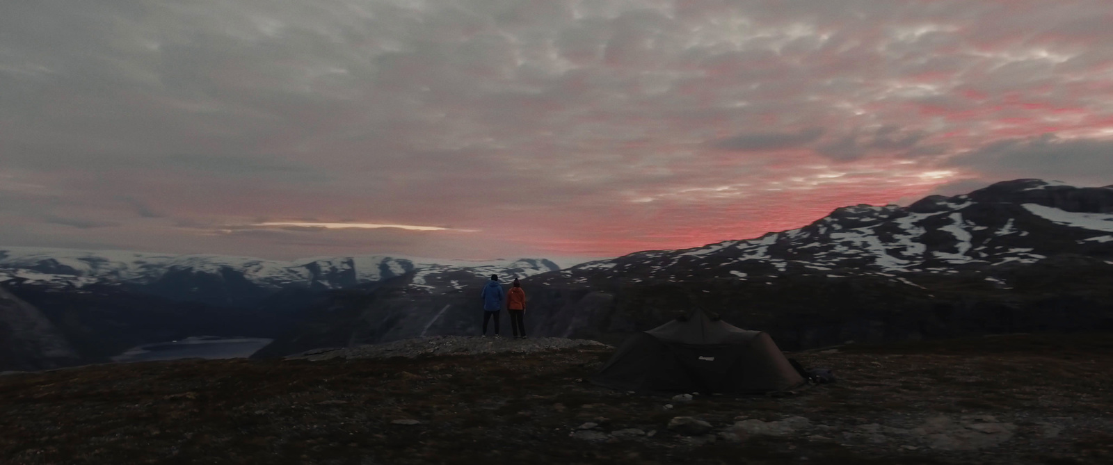 a person standing on top of a mountain with a tent in the background