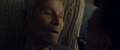 an older man sitting in a chair talking to a younger man