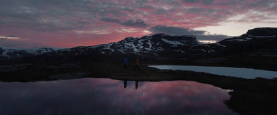 two people standing in front of a lake at sunset