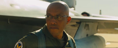 a man with glasses standing in front of a fighter jet