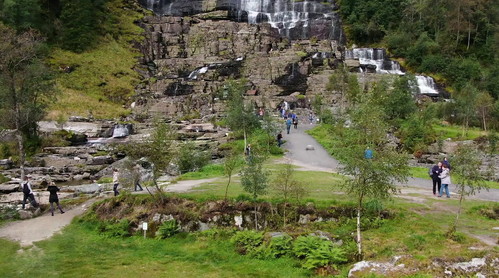 a group of people walking down a path near a waterfall