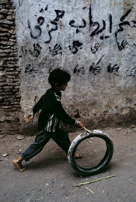 a young boy pushing a tire down a street