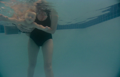 a woman in a black swimsuit holding a baby under water