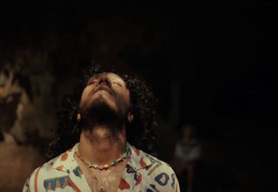 a man with long hair wearing a shirt and a necklace