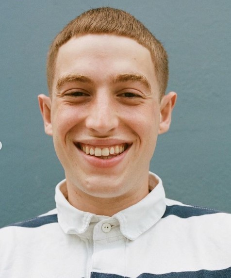 a young man smiling and wearing a striped shirt