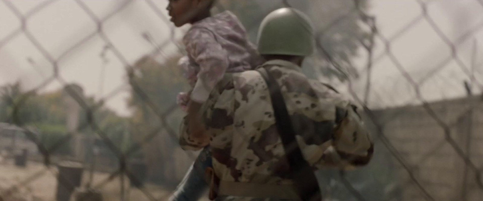 a soldier holding a child behind a chain link fence