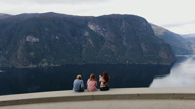 three women sitting on the edge of a cliff overlooking a lake