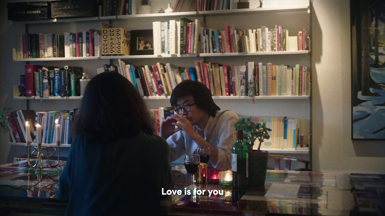 a woman sitting at a table in front of a bookshelf