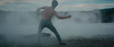 a shirtless man running in the mist near a body of water