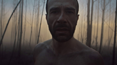 a man with no shirt standing in front of a forest