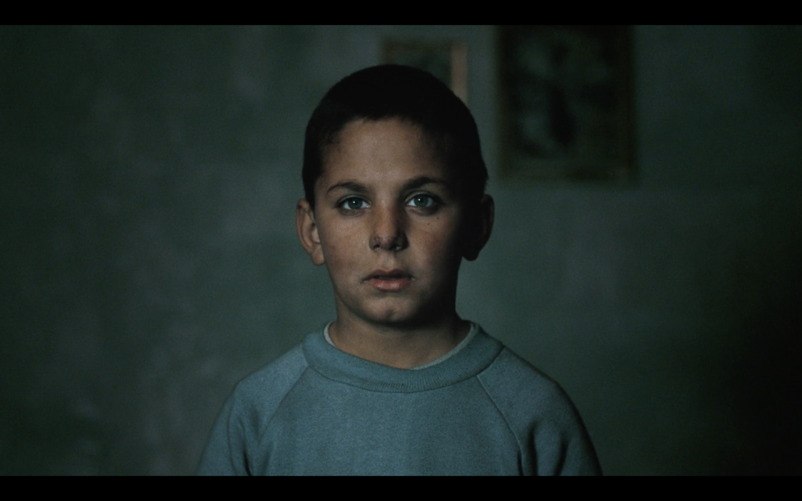 a young boy in a dark room looking at the camera