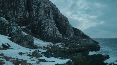 a rocky cliff next to the ocean covered in snow