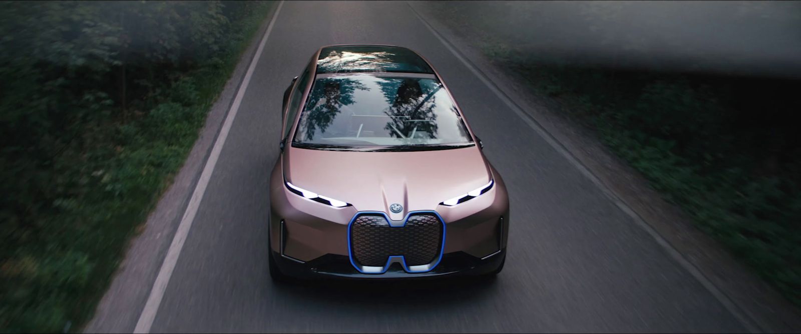 a brown car driving down a road next to a forest