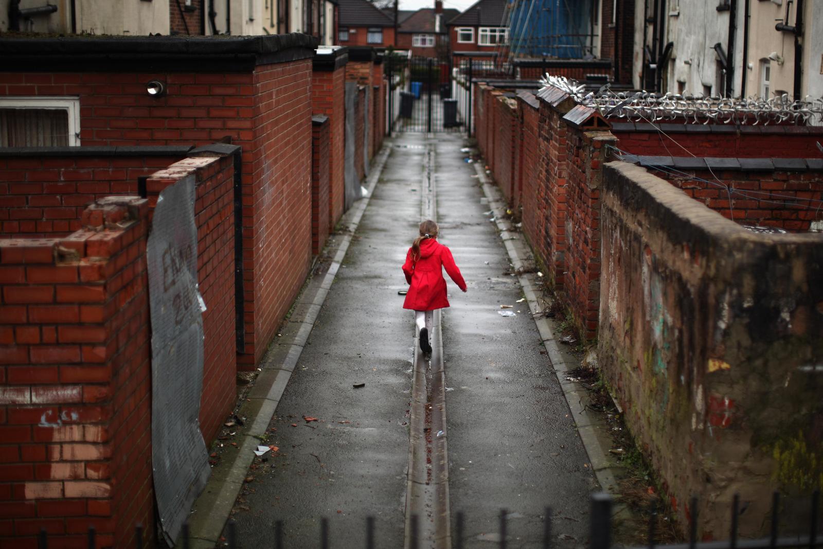 a little girl in a red coat walking down a street