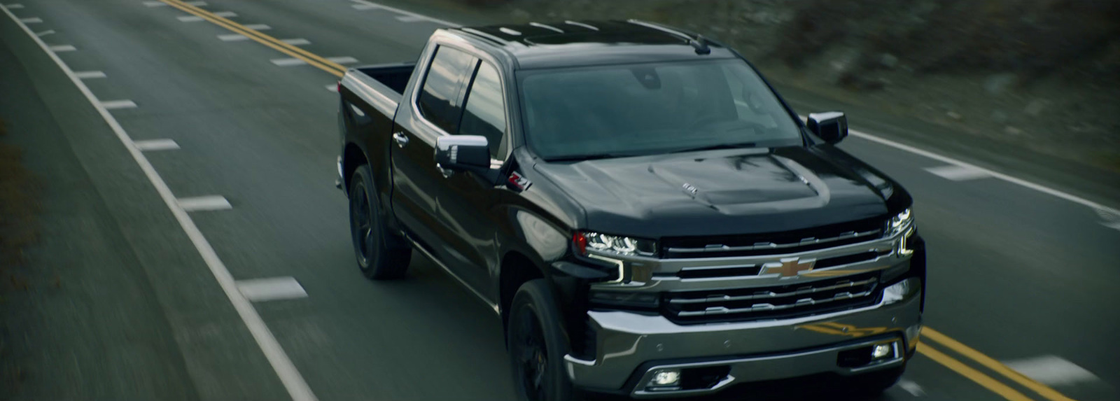 a black truck driving down a road next to a forest