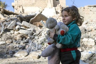 a little girl holding a teddy bear in front of a pile of rubble