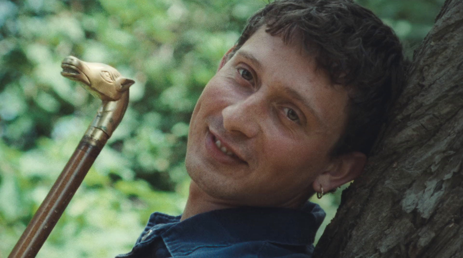 a man leaning against a tree with a cane in his hand