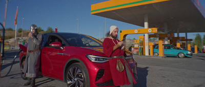 a man standing next to a red car in front of a gas station