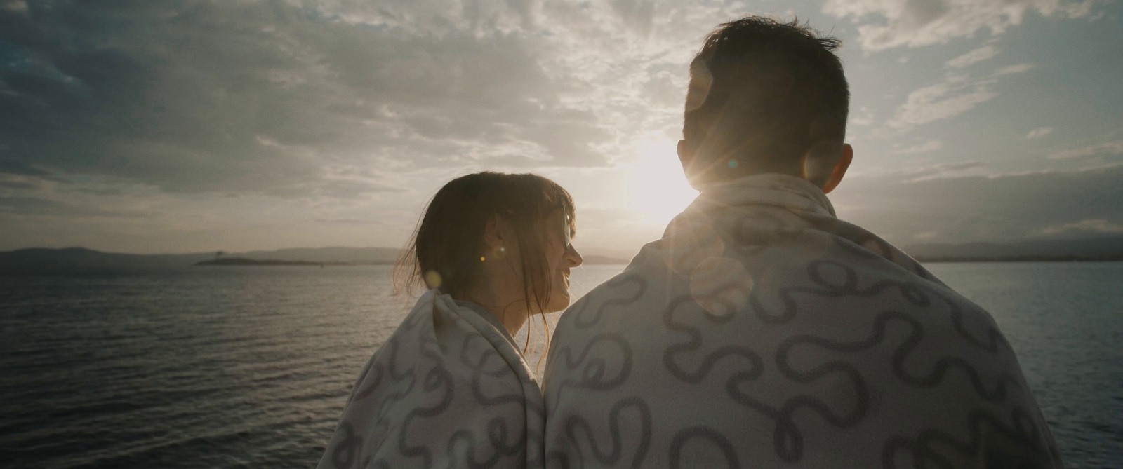 a man and woman wrapped in blankets on a boat at sunset