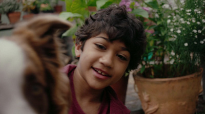 a young boy smiling next to a potted plant