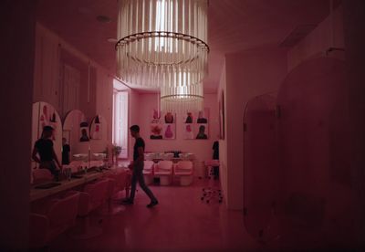 a woman walking through a pink bathroom with a chandelier