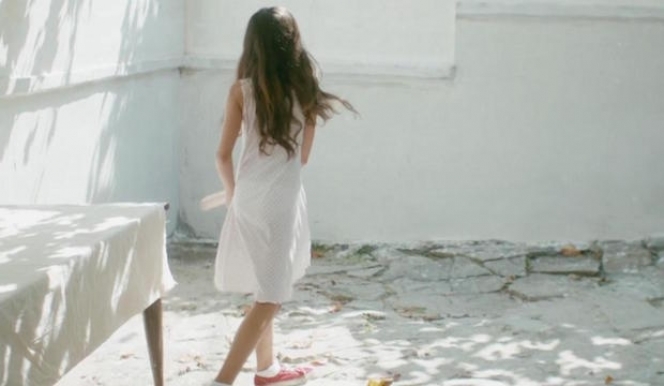 a young girl in a white dress standing in front of a white wall