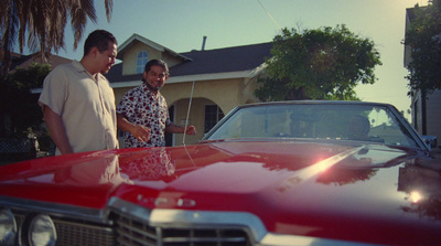 a couple of men standing next to a red car