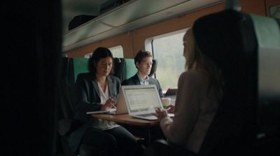 two people sitting on a train looking at a laptop