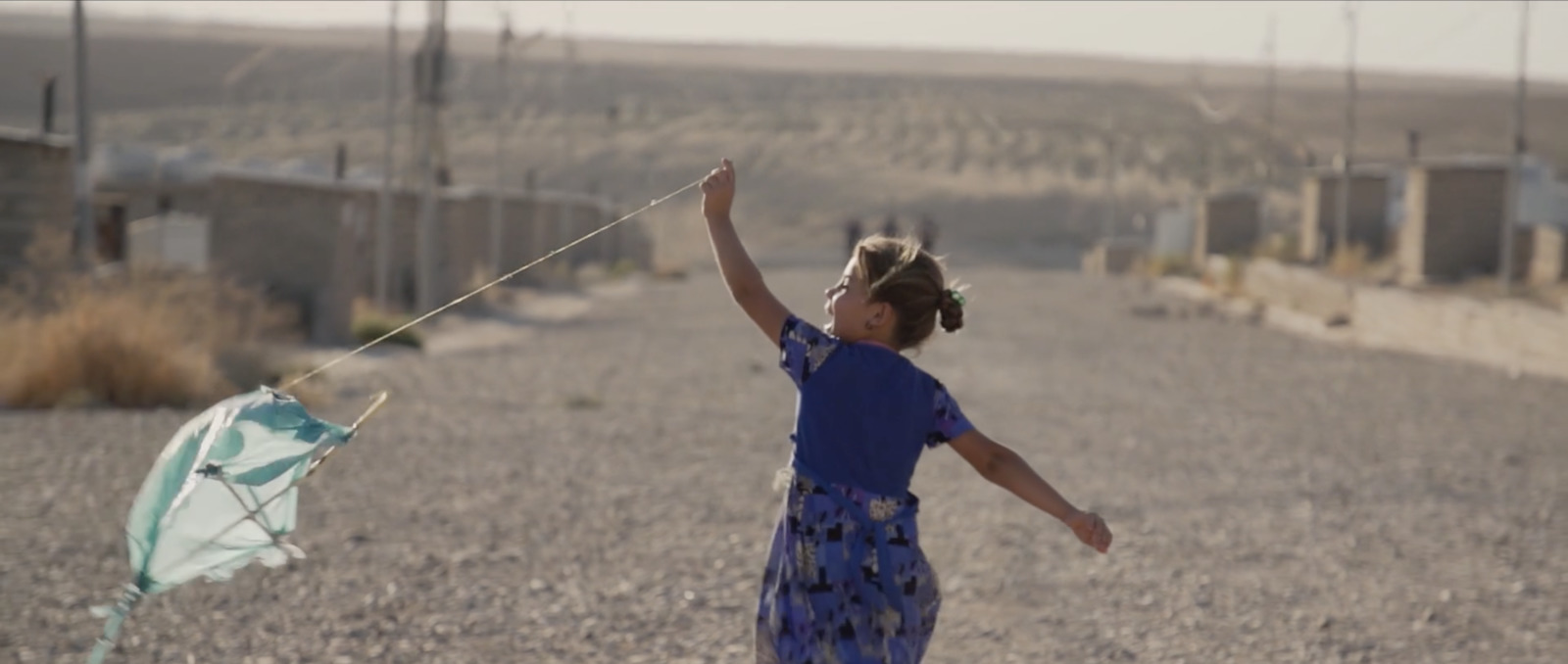 a little girl flying a kite in the middle of a road