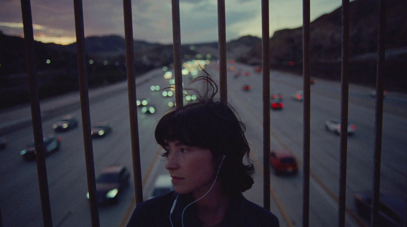 a woman listening to music while standing in front of a fence