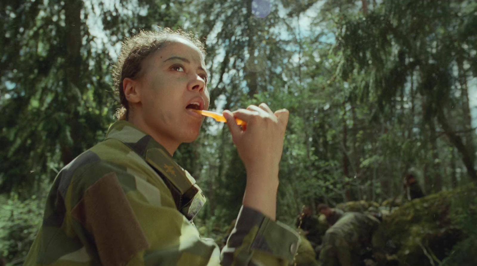 a man in camouflage eating something in a forest