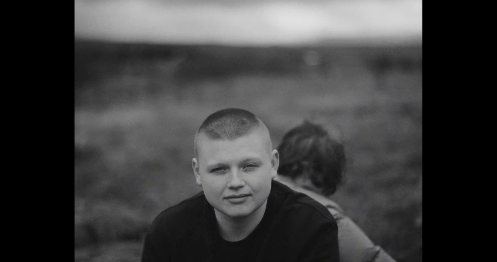 a young man sitting next to a woman in a field