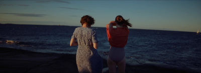 a couple of women standing on top of a beach next to the ocean