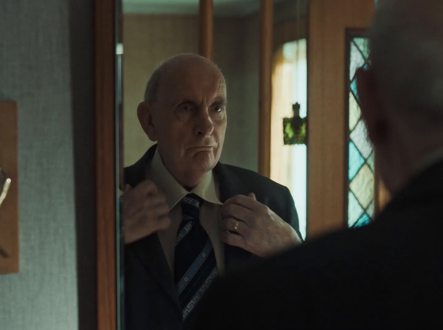 an older man adjusting his tie in front of a mirror