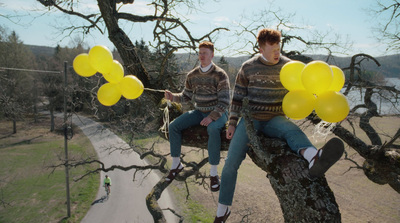 two men sitting on a tree branch with yellow balloons