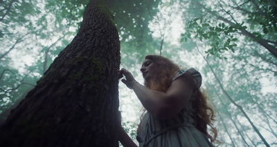 a woman standing next to a tree in a forest